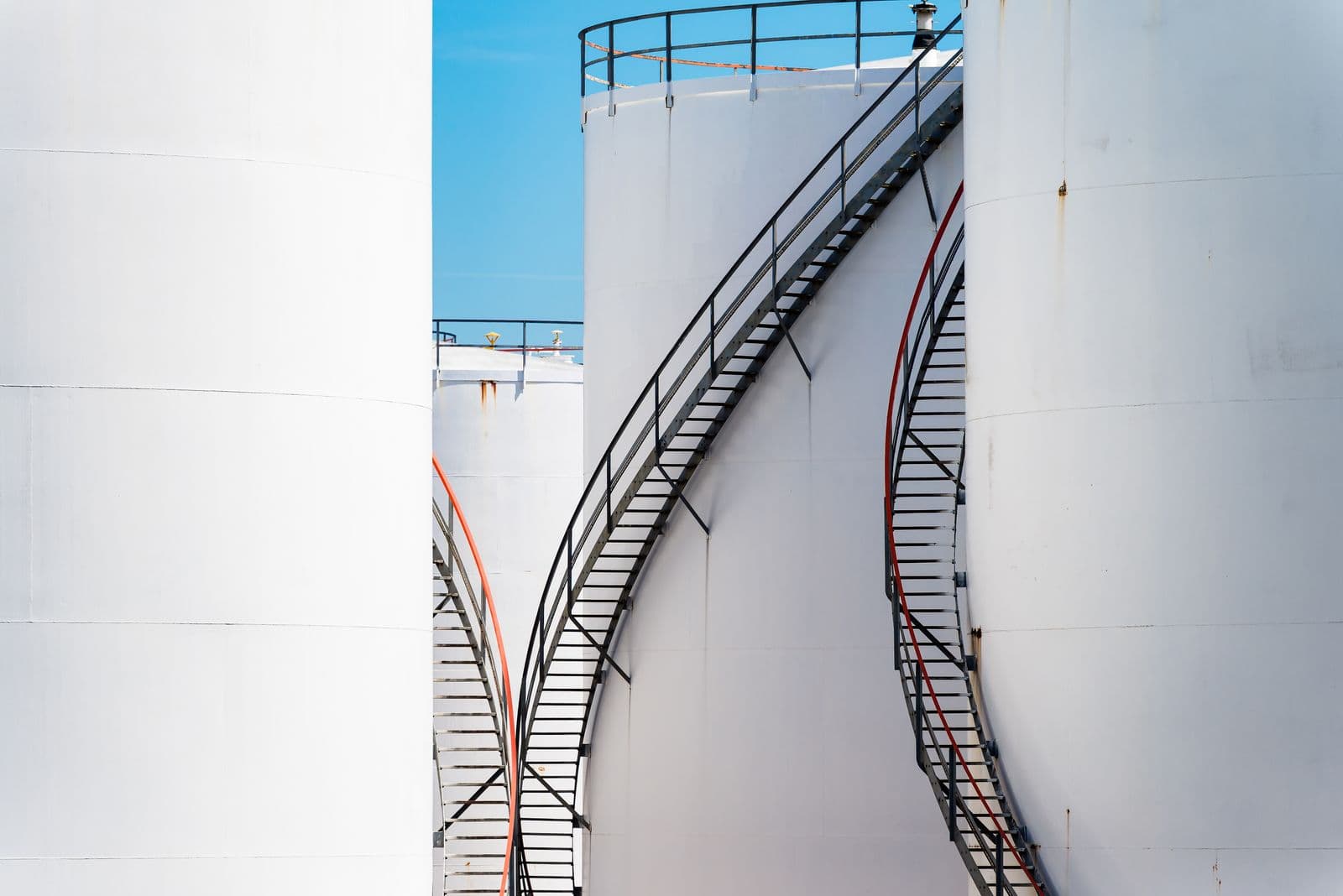 A row of large white aboveground oil storage tanks with access stairs at an industrial site.
