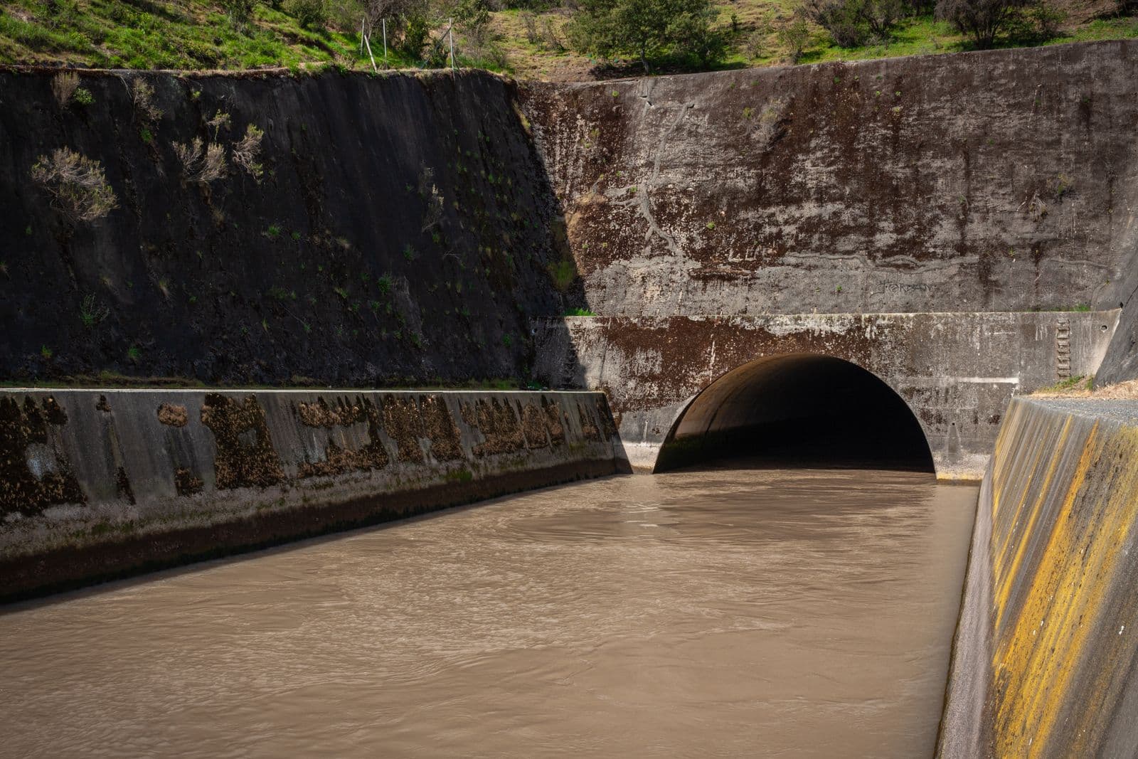 A large concrete storm-drain culvert carrying runoff water into a tunnel.